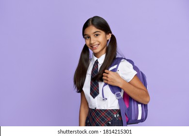 Happy smiling indian preteen girl, latin kid schoolgirl with ponytails wears uniform holding backpack standing isolated on lilac violet background looking at camera, back to school concept, portrait.