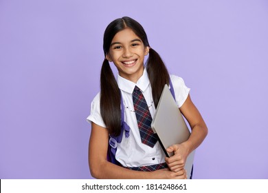 Happy smiling indian preteen girl, latin kid wears school uniform holding backpack and laptop computer isolated on lilac violet background looking at camera, remote learning online concept, portrait.