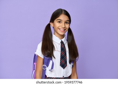 Happy smiling indian schoolgirl in school uniform with backpack bag standing isolated on violet lilac background looking at camera. Portrait of smart latin hispanic girl kid student.