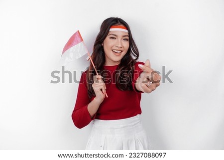 Happy smiling Indonesian woman holding Indonesia's flag and showing love sign to celebrate Indonesia Independence Day isolated over white background.