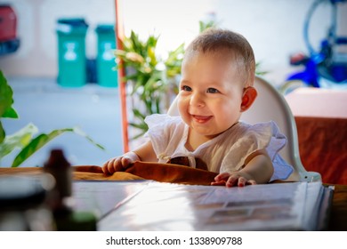 Happy Smiling Infant Girl Is Sitting On A Baby High Chair In Restaurant. 