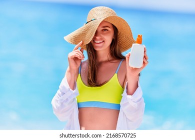 Happy Smiling Joyful Carefree Caucasian Female Holding White Empty Bottle Blank Of Sunscreen Spray On Sea Beach In Sunny Summer Day. Sun Protection