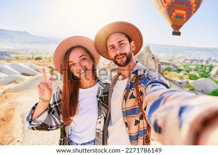 Happy smiling joyful traveling couple takes selfie photo in Nevsehir, Goreme. Beautiful destination with colorful flying hot air balloons in Anatolia, Kapadokya