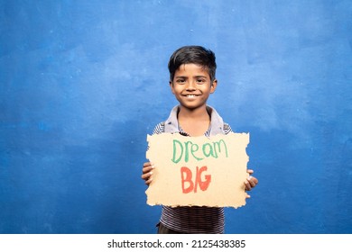 Happy smiling kid with dream big sign board standing against blue background by looking at camera - concept of motivation, inspirational and childhood aspirations. - Powered by Shutterstock