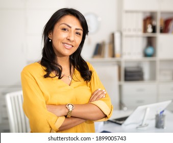 Happy smiling Latin American businesswoman standing in office with arms crossed looking at camera - Shutterstock ID 1899005743