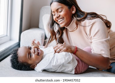 Happy smiling laughing Indian mother playing with black baby girl daughter. Family mixed race people mom and kid together hugging at home. Authentic candid lifestyle with infant kid child. 