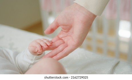 Happy Smiling Little Baby Laying Down On The Bed While Some Adult Playing From Above Concept Of Nursing Care Motherhood And Baby Childhood