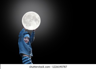 Happy Smiling Little Boy Child Wearing Hoodie Holding Glowing Full Moon In His Hands And Looking At Camera Isolated On Black Background With Copy Space For Text.