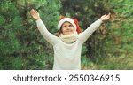 Happy smiling little girl child in santa red hat enjoying snow in snowy forest on Christmas tree background