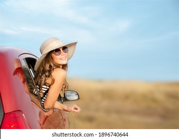 Happy Smiling Little Girl Child Goes To Summer Travel Trip In The Red Car. Preteen In Hat And Sunglasses Enjoying Road Trip. 