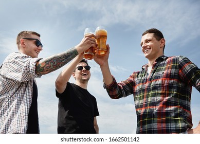 Happy smiling male friends drinking beer and clinking glasses at bar or pub on rooftop, copy space. Friendship and celebration concept 