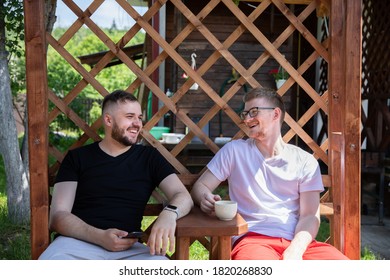 Happy Smiling Male Friends Resting Outdoors, Two Handsome Guys Sitting On Back Yard Of Coutry House, Men Talking And Laughing On Summer Weekend. People, Positive Emotions, Fun, Leisure Time Concept