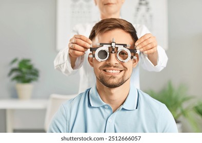 Happy, smiling male patient getting eye check at optometrist's office. Optometrist uses specialized ophthalmic equipment to test eyesight of young man who needs prescription glasses. Optometry concept - Powered by Shutterstock