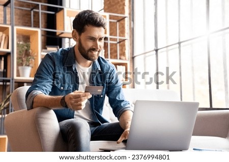 Happy smiling man buying, shopping or paying online with bank card and laptop. Male customer doing internet purchase using web banking service looking at computer screen making secure payment