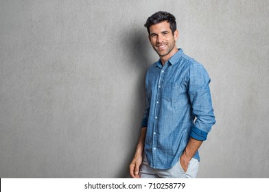 Happy smiling man leaning against grey wall. Portrait of proud mid man isolated on grey background. Young casual hispanic man against grey wall looking at camera.