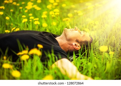 Happy smiling man lying on grass with yellow dandelion at sunny day - Powered by Shutterstock