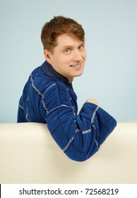 Happy Smiling Man Sitting On A Couch In His Dressing Gown On Blue