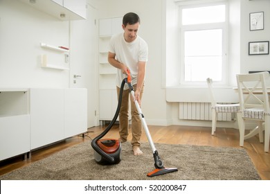 Happy Smiling Man Vacuum Cleaning The Carpet In The Living Room, Modern Scandinavian Interior. Busy, Cleaning Day. Home, Housekeeping Concept. 