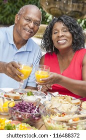 A happy, smiling man and woman senior African American couple drinking orange juice & eating healthy food at a picnic table outside