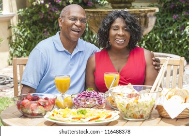A happy, smiling man and woman senior African American couple eating healthy food at a picnic table outside
