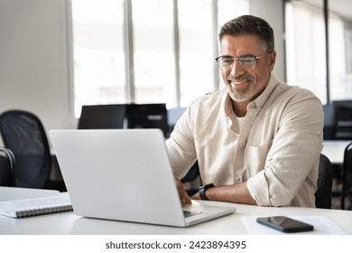 Happy smiling mature Indian or Latin business man ceo trader using computer, typing, working in modern office, doing online data market analysis, thinking planning tech strategy looking at laptop. - Powered by Shutterstock