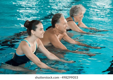 Happy Smiling Mature Man And Old Woman Cycling On A Water Bike In Swimming Pool. Happy And Healthy Senior People Doing Aqua Aerobics On Exercise Bikes In A Swimming Pool. Fitness Class Training.
