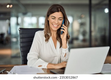 Feliz sonriente mujer madura de negocios de mediana edad, mujer ejecutiva profesional de 40 años hablando por teléfono haciendo una llamada de negocios en el teléfono celular en el trabajo en la oficina usando computadora portátil.