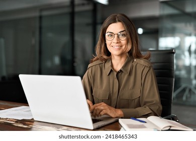 Happy smiling mature middle aged professional business woman investor manager executive or lawyer attorney adviser looking at camera at workplace working on laptop computer in office, portrait. - Powered by Shutterstock