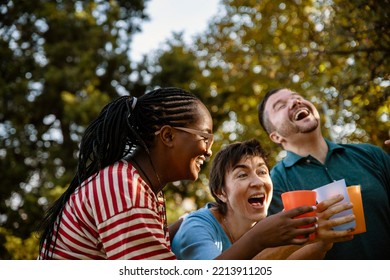 Happy Smiling Mature Mother With Her Son And Daughter In Low, Cheers With Glasses Outdoors. Cheerful Family Reunion In Picnic Day