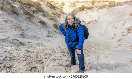 Happy and smiling mature woman pausing while climbing a coastal dune among white sand and wild grass, sunny day in Hargen aan Zee, North Holland, Netherlands. Active life concept - Powered by Shutterstock