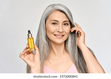 Happy Smiling Mid Age Asian Attractive Woman With Grey Silky Shiny Volume Hair Holding Bottle With Serum Essence Liquid Oil For Antiaging Skincare And Haircare. Cosmetics Hair Face Treatment Concept.