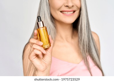 Happy Smiling Mid Age Asian Attractive Woman With Grey Hair Holding In Hand Bottle With Serum Essence Hyaluronic Hydrate Oil For Skincare And Haircare. Hair Face Treatment Concept.