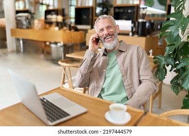 Happy smiling middle aged professional business man, older mature entrepreneur sitting at cafe table talking on cell phone making mobile call remote working online on laptop and having morning coffee. - Powered by Shutterstock