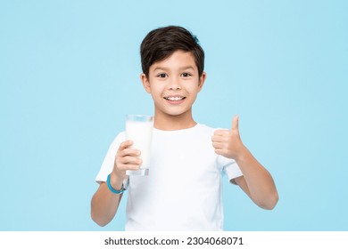 Happy smiling mixed race Asian kid boy holding a glass of fresh milk and giving thumbs up in isolated light blue color background studio shot - Powered by Shutterstock