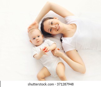 Happy Smiling Mother And Baby Lying On Bed At Home, Top View