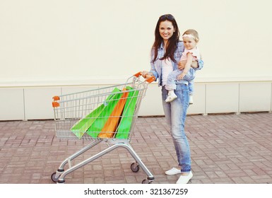 Happy Smiling Mother And Baby With Trolley Cart And Colorful Shopping Bags