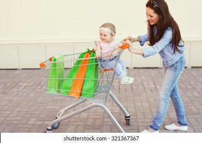 Happy Smiling Mother And Child With Trolley Cart And Colorful Shopping Bags Having Fun