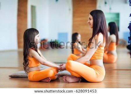 Happy smiling mother and daughter in bright orange sport suits sitting on the floor in the gym