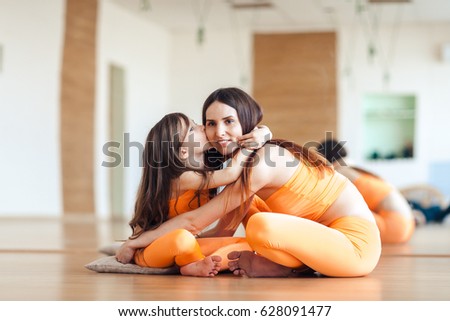 Happy smiling mother and daughter in bright orange sport suits sitting on the floor in the gym, hugging, looking at the camera
