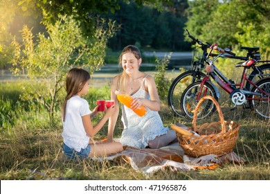 Happy smiling mother and daughter drinking orange juice at picnic - Powered by Shutterstock