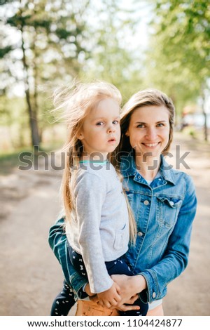 Happy smiling mother hugging her lovely little daughter outdoor. Lifestyle family. Adult cheerful female parent playing with her beautiful emotional child at nature in summer. Positive people faces