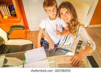 Happy Smiling Mother Sititng At The Desk With Son At Her Lap, Peaceful Mom Using Modern Computer, Work From Home At Quarantine Time, Coronavirus Pandemia Lifestyle, Parenting, Upbringing