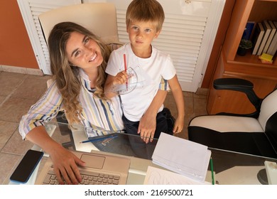 Happy Smiling Mother Sititng At The Desk With Son At Her Lap, Peaceful Mom Using Modern Computer, Work From Home At Quarantine Time, Coronavirus Pandemia Lifestyle, Parenting, Upbringing