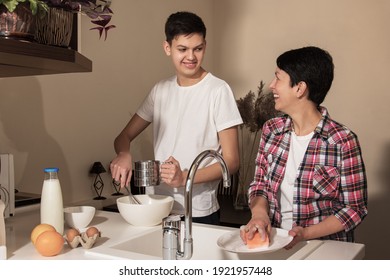 Happy smiling mother and son on kitchen. Teenage boy helping to cook food, mom washing the dishes. Concept of friendly relationship between parents and children teenagers - Powered by Shutterstock