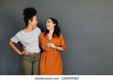 Happy smiling multiethnic women embracing each other against grey wall with copy space. Happy laughing girls standing on grey background and looking at each other. Carefree girls having fun. - Powered by Shutterstock