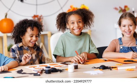 Happy Smiling Multinational Group Of Children  Making Halloween Home Decorations Together, Kids Painting Pumpkins And Making Paper Cuttings