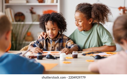 Happy Smiling Multinational Group Of Children  Making Halloween Home Decorations Together, Kids Painting Pumpkins And Making Paper Cuttings