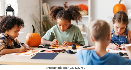 Happy Smiling Multinational Group Of Children  Making Halloween Home Decorations Together, Kids Painting Pumpkins And Making Paper Cuttings