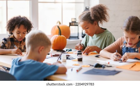 Happy Smiling Multinational Group Of Children  Making Halloween Home Decorations Together, Kids Painting Pumpkins And Making Paper Cuttings