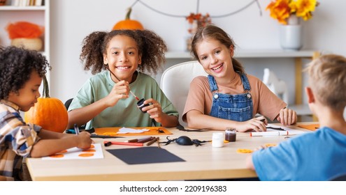 Happy Smiling Multinational Group Of Children  Making Halloween Home Decorations Together, Kids Painting Pumpkins And Making Paper Cuttings